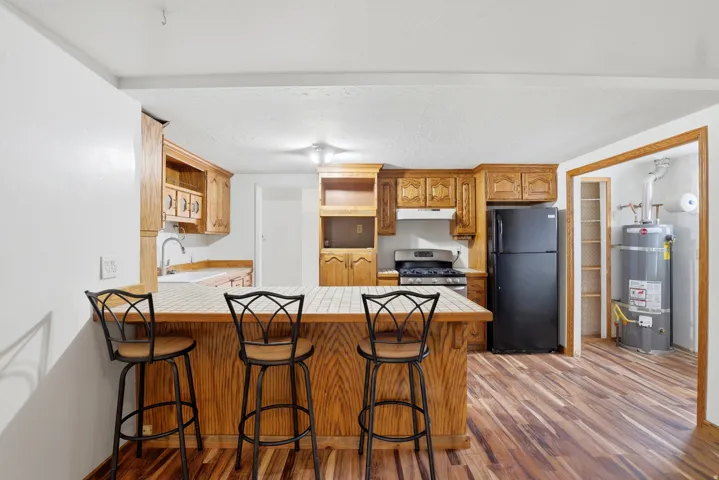 Kitchen with a breakfast bar, freestanding refrigerator, a peninsula, light wood finished floors, and wood finish cabinetry