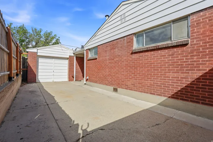 View of side of property featuring concrete driveway, crawl space, brick siding, a garage, and an outdoor structure
