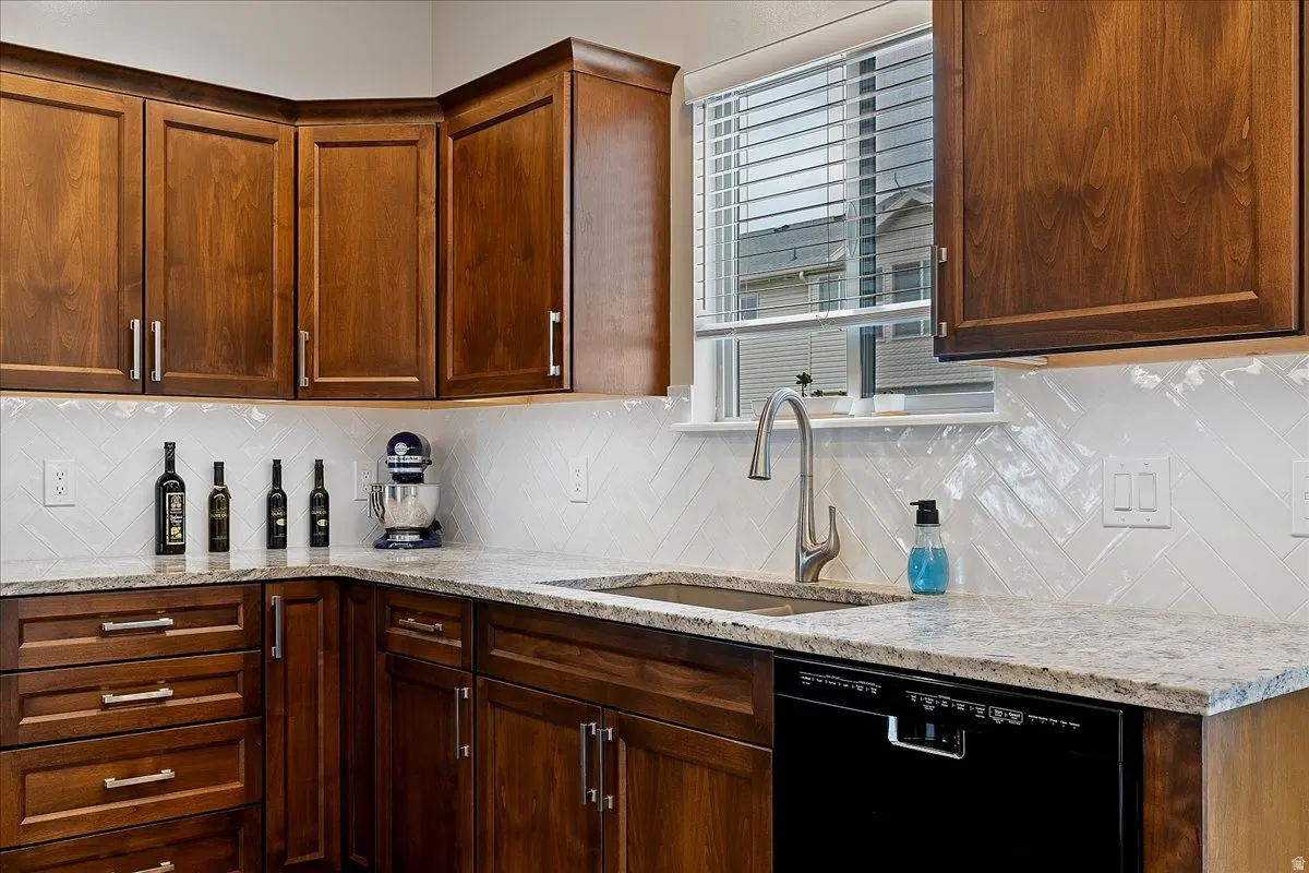 Kitchen with light stone counters, backsplash, and black dishwasher