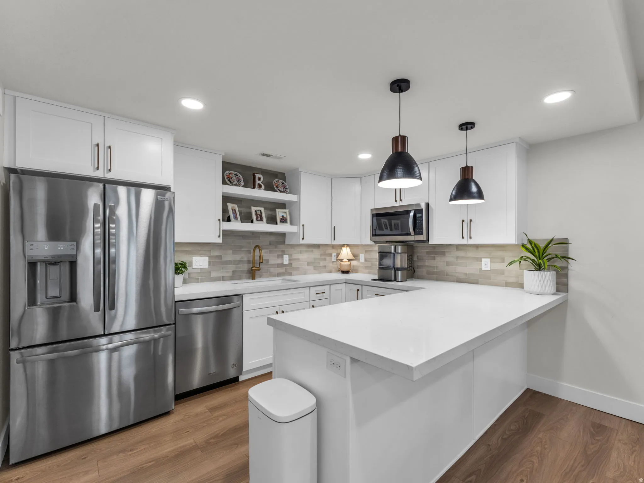 Kitchen with stainless steel appliances, open shelves, a peninsula, wood finished floors, and white cabinets