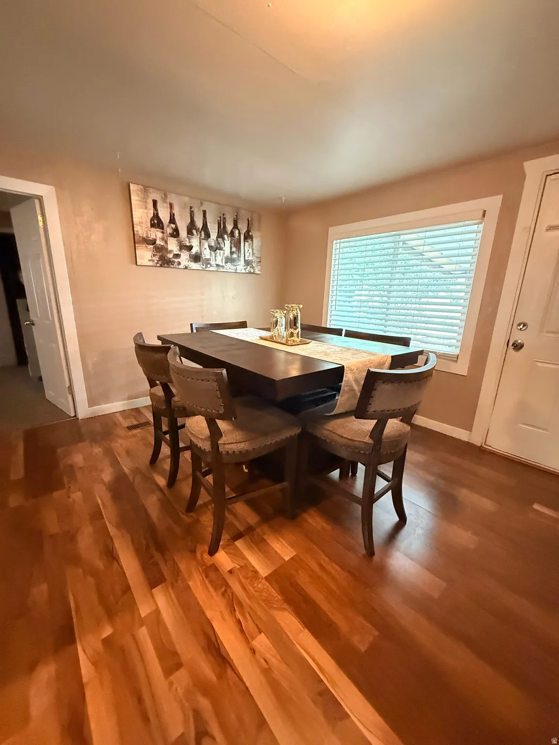 Wood-finish flooring with varied plank tones, a window with horizontal blinds, and a white interior door with a silver-tone knob