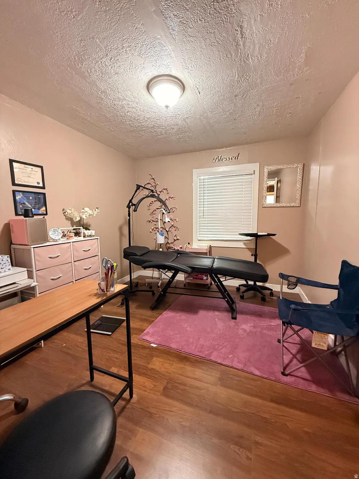 Versatile home office featuring wood-finish flooring, recessed ceiling lighting, and ample natural light from a large window with plantation shutters