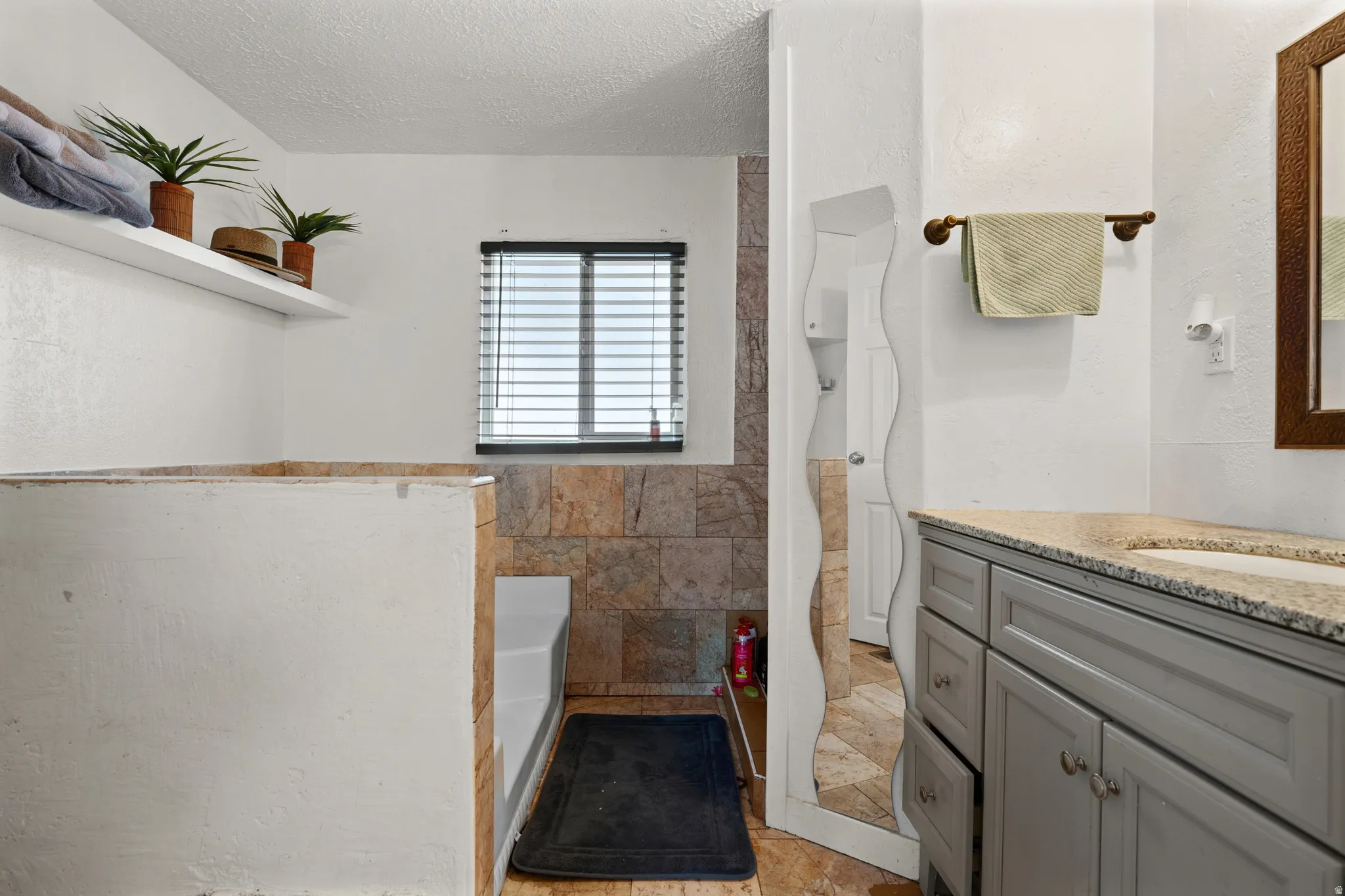 Bathroom with vanity, a textured ceiling, a shower with shower curtain, a tub to relax in, and tile walls