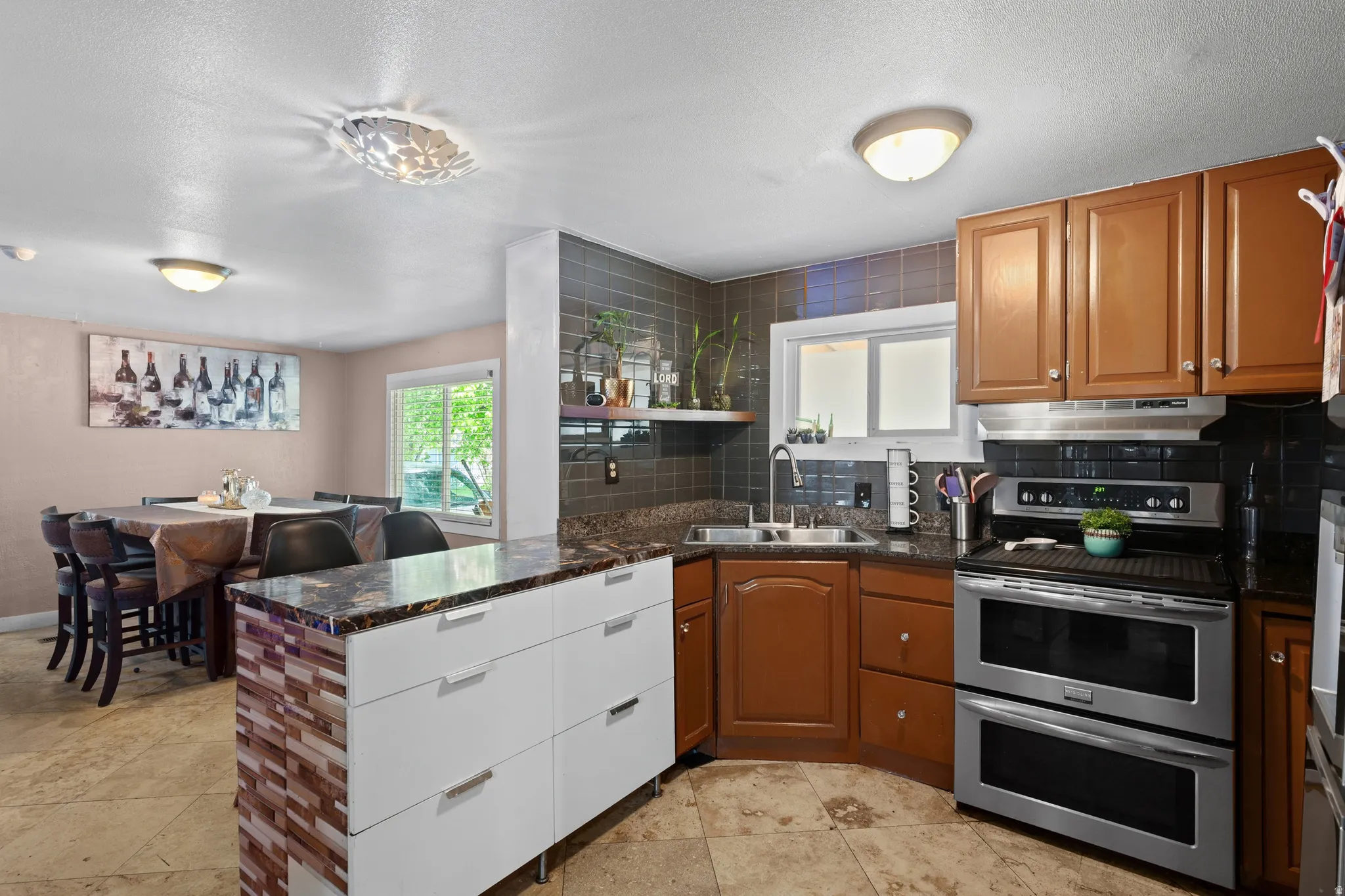 Kitchen with a peninsula, decorative backsplash, range with two ovens, wood finish cabinetry, and a textured ceiling