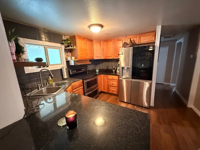 Kitchen featuring wood-finish cabinetry, dark stone countertops, a stainless steel double-basin sink with gooseneck faucet, a built-in double oven, and a stainless steel refrigerator