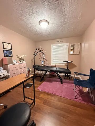 Versatile home office featuring wood-finish flooring, recessed ceiling lighting, and ample natural light from a large window with plantation shutters