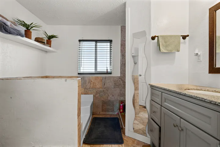 Bathroom with vanity, a textured ceiling, a shower with shower curtain, a tub to relax in, and tile walls