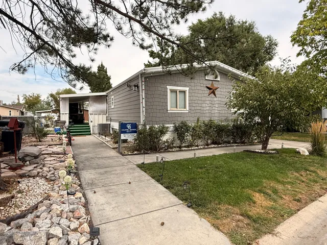 Gray shingle siding with white trim, concrete walkway, landscaped rock garden, and a green lawn