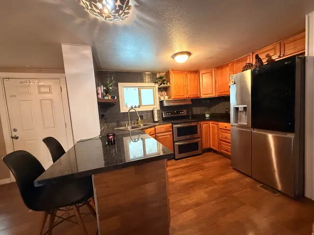 Kitchen featuring wood-finish flooring, a dark stone-finish island with seating, wood cabinetry, stainless steel appliances, and a dark tile backsplash