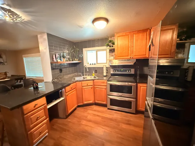 Wood-finish flooring, custom cabinetry, stainless steel appliances, dark stone countertops, and a subway tile backsplash