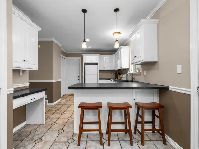 Kitchen featuring a breakfast bar, ornamental molding, dark countertops, white cabinets, and freestanding refrigerator