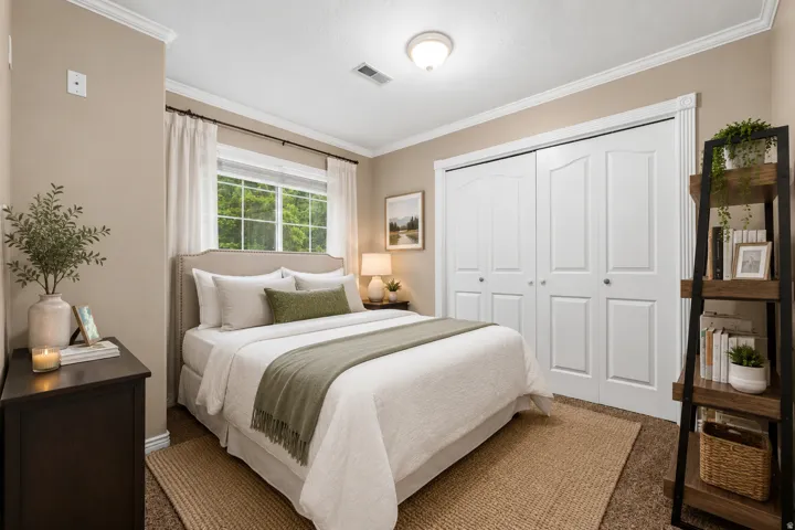 Bedroom featuring a window with exterior tree views, bi-fold closet doors, crown molding, and a neutral color palette