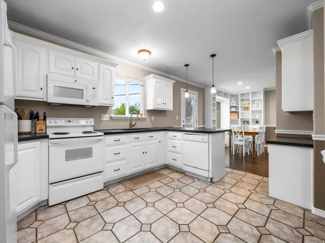 Kitchen with a peninsula, white appliances, ornamental molding, dark countertops, and pendant lighting