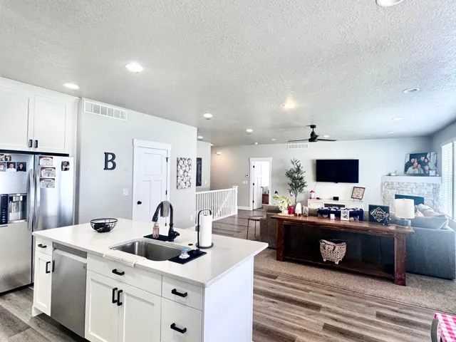 Kitchen featuring a kitchen island with sink, open floor plan, light wood finished floors, white cabinetry, and stainless steel appliances