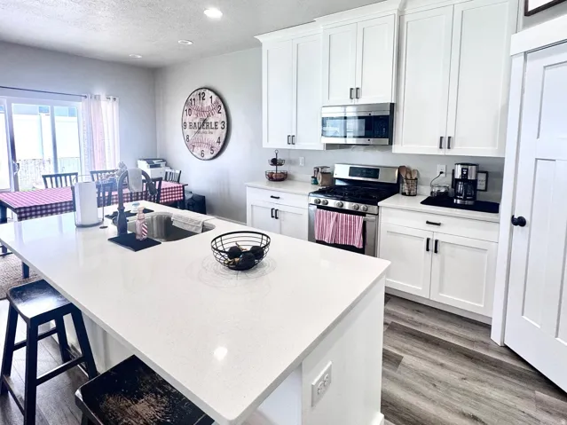 Kitchen featuring a kitchen breakfast bar, an island with sink, white cabinetry, stainless steel appliances, and a textured ceiling
