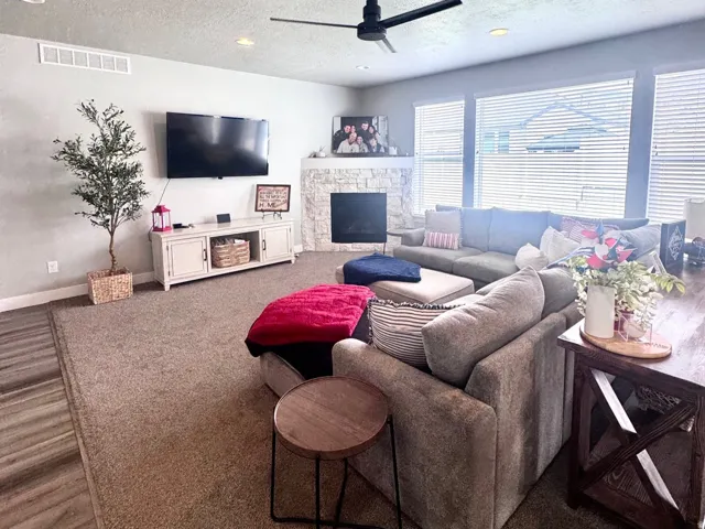 Living room featuring a textured ceiling, ceiling fan, a stone fireplace, and wood finished floors