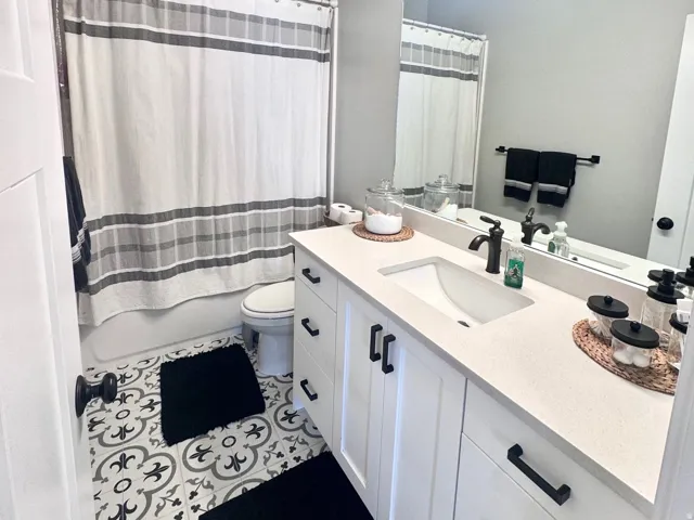 Bathroom with vanity, shower / bath combo with shower curtain, a textured ceiling, and dark tile patterned flooring