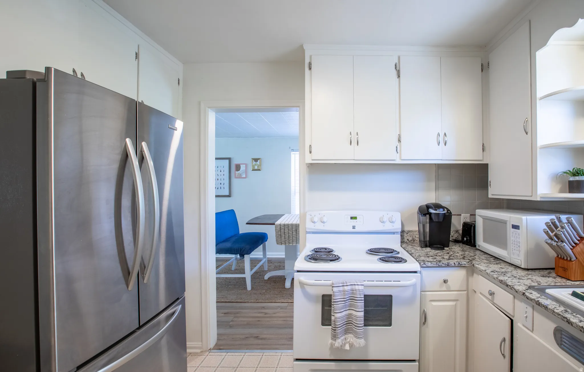 Kitchen with white appliances, white cabinetry, decorative backsplash, light stone countertops, and light tile patterned floors