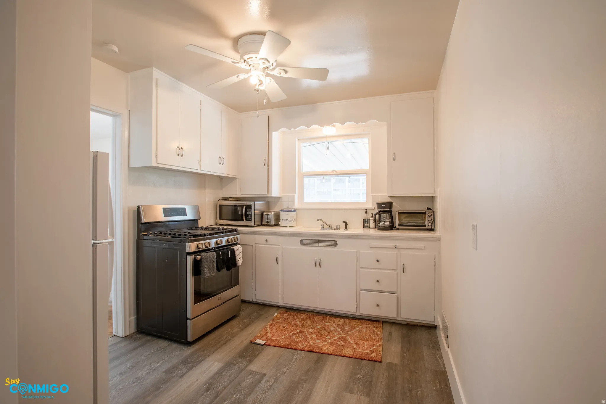 Kitchen featuring stainless steel appliances, white cabinetry, light countertops, and dark wood-style flooring