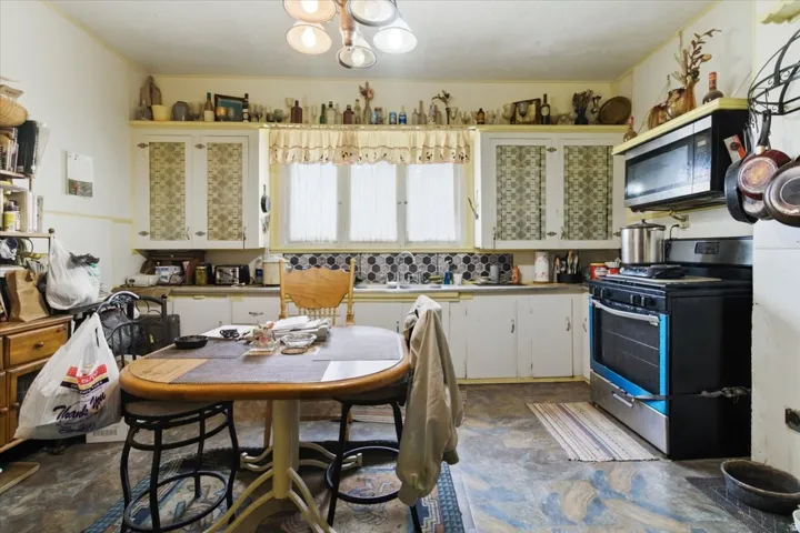 Kitchen featuring stainless steel appliances, white cabinetry, hanging lights, and crown molding
