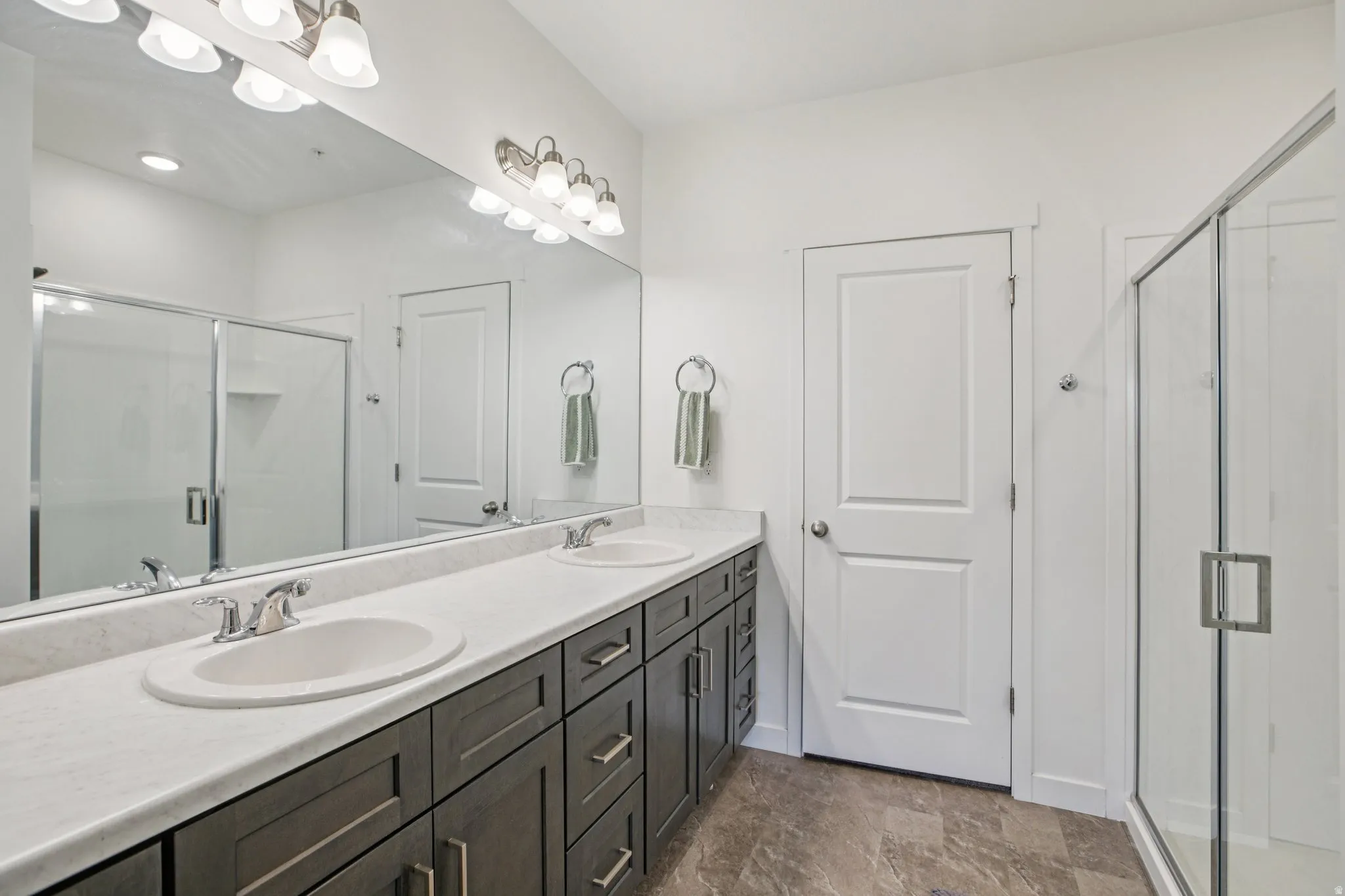 Bathroom with a shower stall, double vanity, and stone finish floors