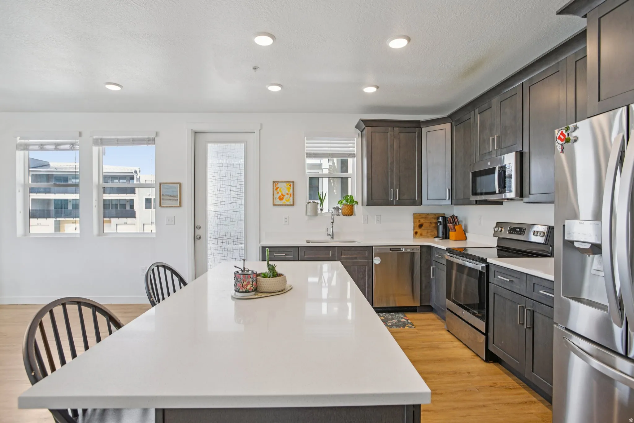 Kitchen featuring stainless steel appliances, light wood-style floors, dark wood finish cabinets, recessed lighting, and light stone counters