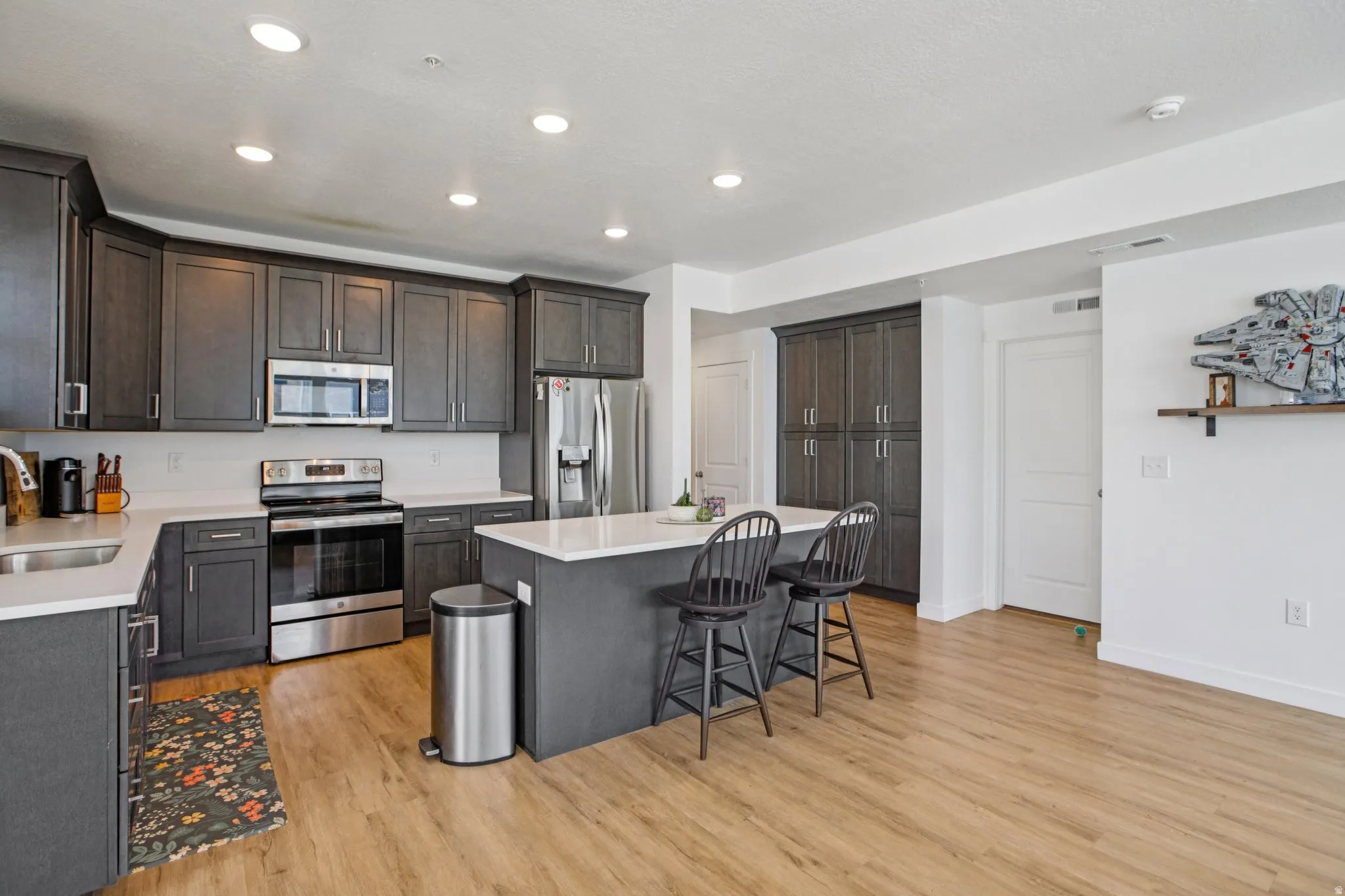 Kitchen with stainless steel appliances, a kitchen bar, dark wood finish cabinets, light wood-type flooring, and a center island
