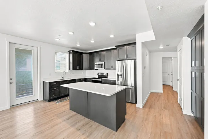 Kitchen featuring dark wood-finish cabinetry, stainless steel appliances, a white island with countertop, recessed lighting, and wood-finish flooring