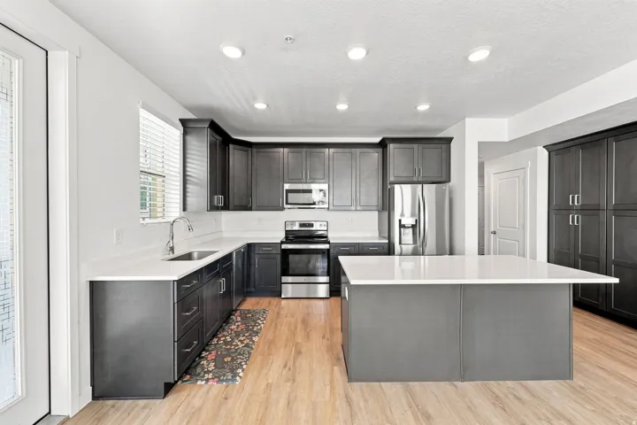 Contemporary kitchen featuring dark wood-finish cabinetry, stainless steel appliances, a center island with a light-toned countertop, and light wood-finish flooring