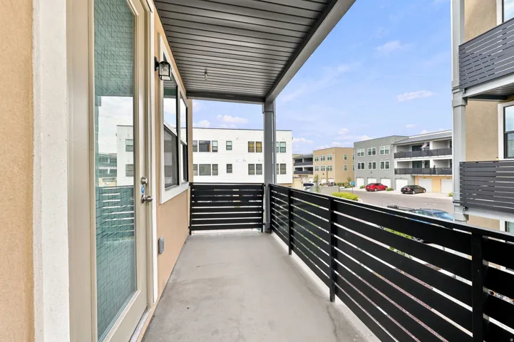 Covered outdoor balcony with a concrete floor, black slatted railing, and stucco exterior walls