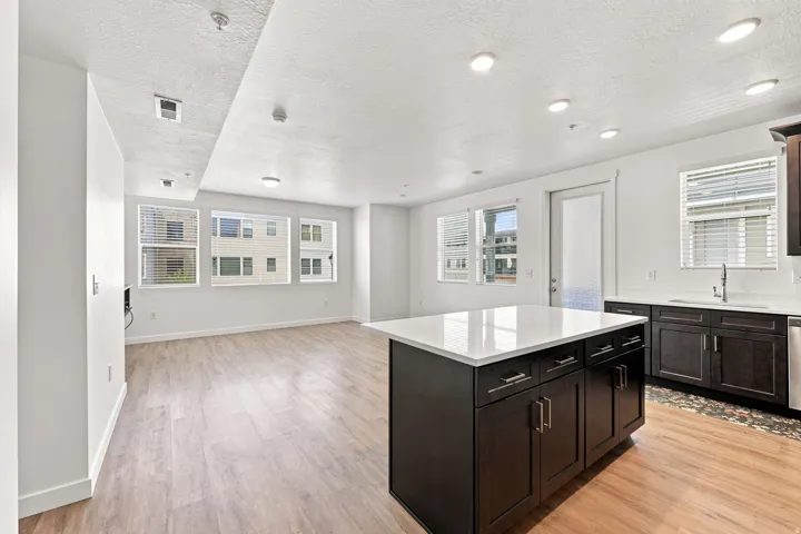 Open-concept living area with wood-finish flooring, recessed lighting, multiple windows, a kitchen island with a light-colored countertop, and dark wood cabinetry