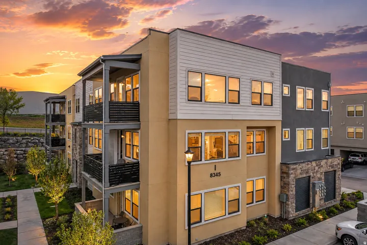 Multi-story building featuring balconies with horizontal railings, extensive window coverage, and exterior lighting