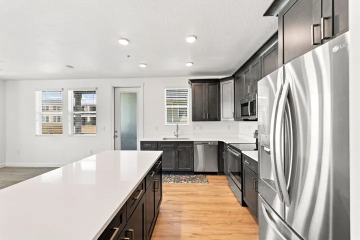 Spacious kitchen featuring a large island with a white countertop, dark wood-finish cabinetry, stainless steel appliances, and wood-finish flooring