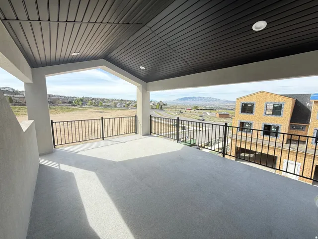 Spacious covered balcony featuring a textured concrete floor, black metal railings, recessed lighting, and a panoramic mountain backdrop
