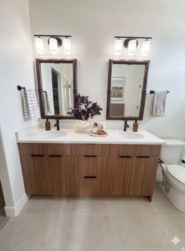 Dual wood-finish vanity with integrated sinks, quartz-finish countertop, dark-framed mirrors, and contemporary light fixtures