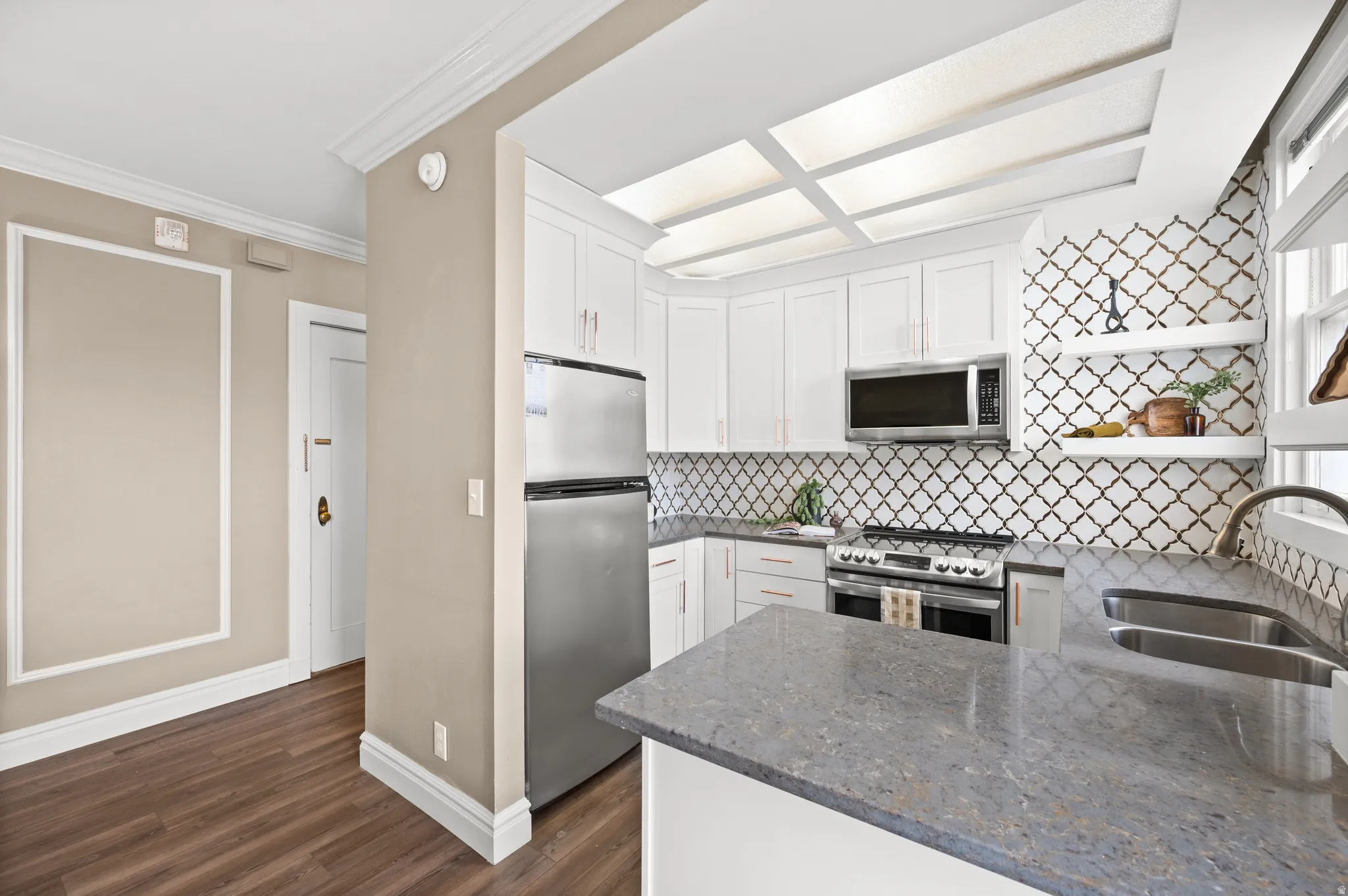 Kitchen featuring dark stone countertops, white cabinetry, ornamental molding, stainless steel appliances, and open shelves