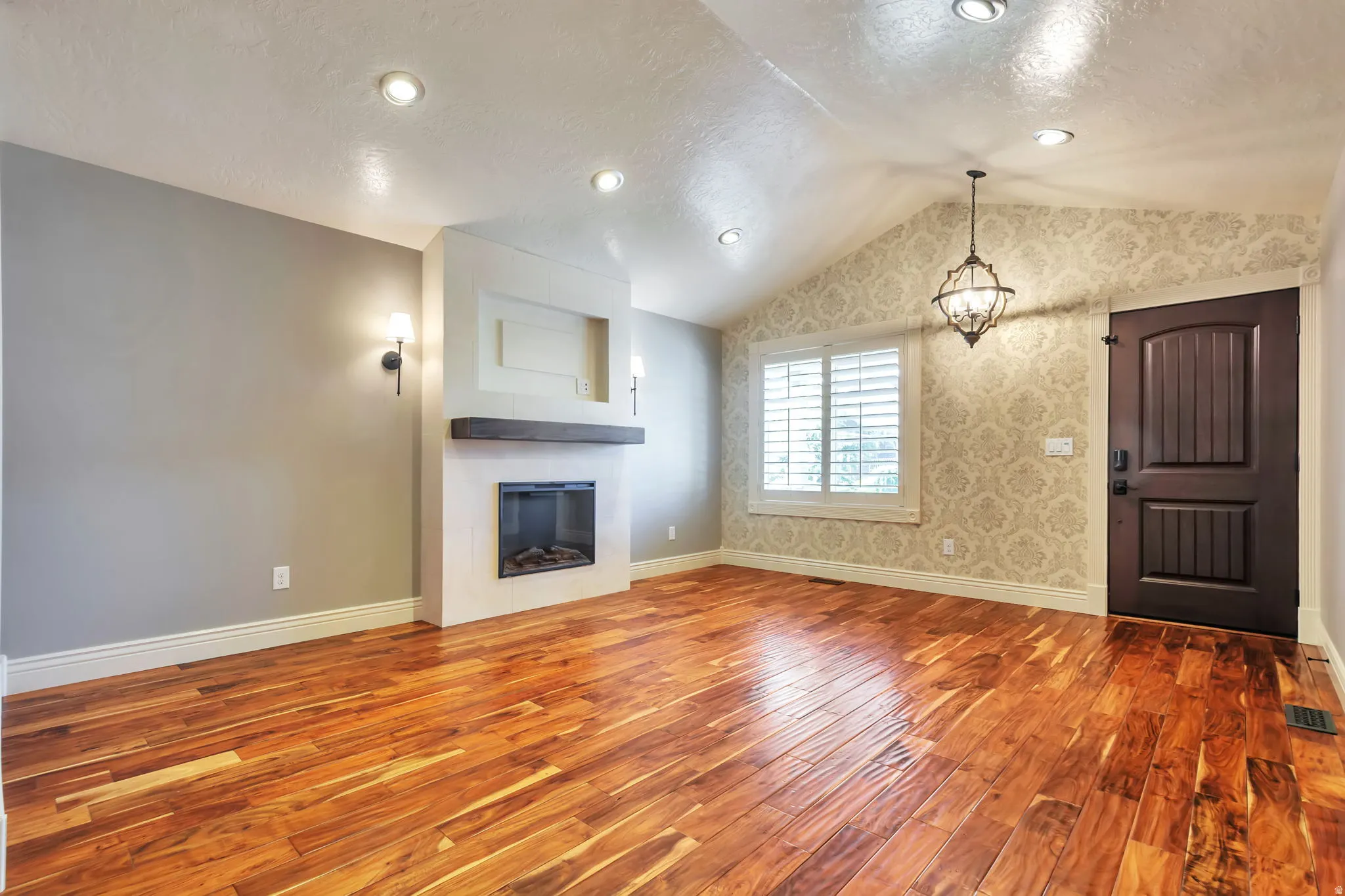 Unfurnished living room with wood finished floors, a textured ceiling, a glass covered fireplace, and hanging lights