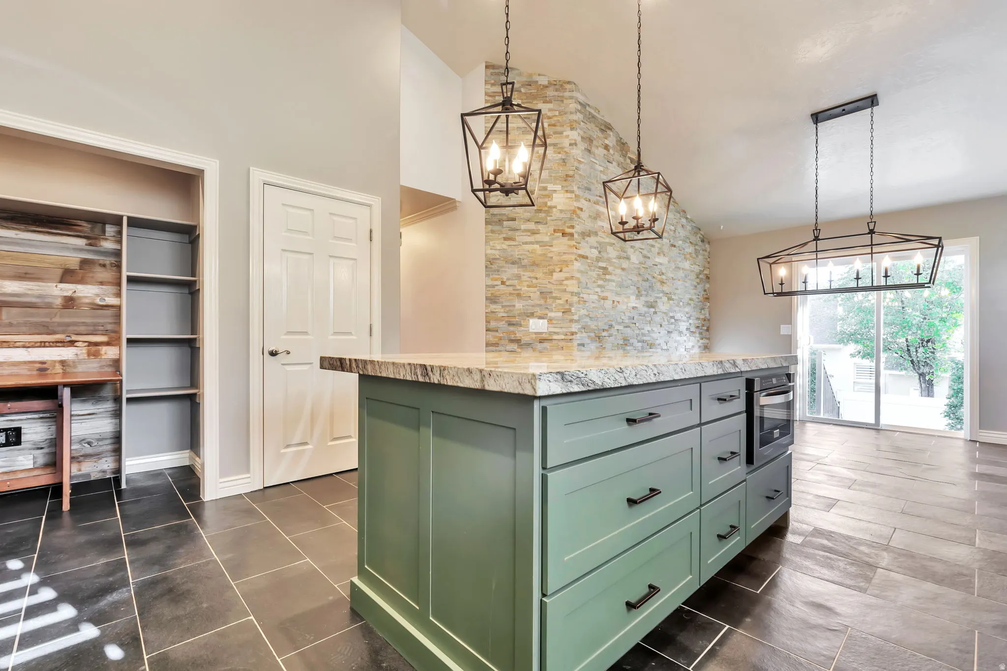 Kitchen featuring green cabinetry, a kitchen island, a chandelier, stainless steel oven, and light stone counters