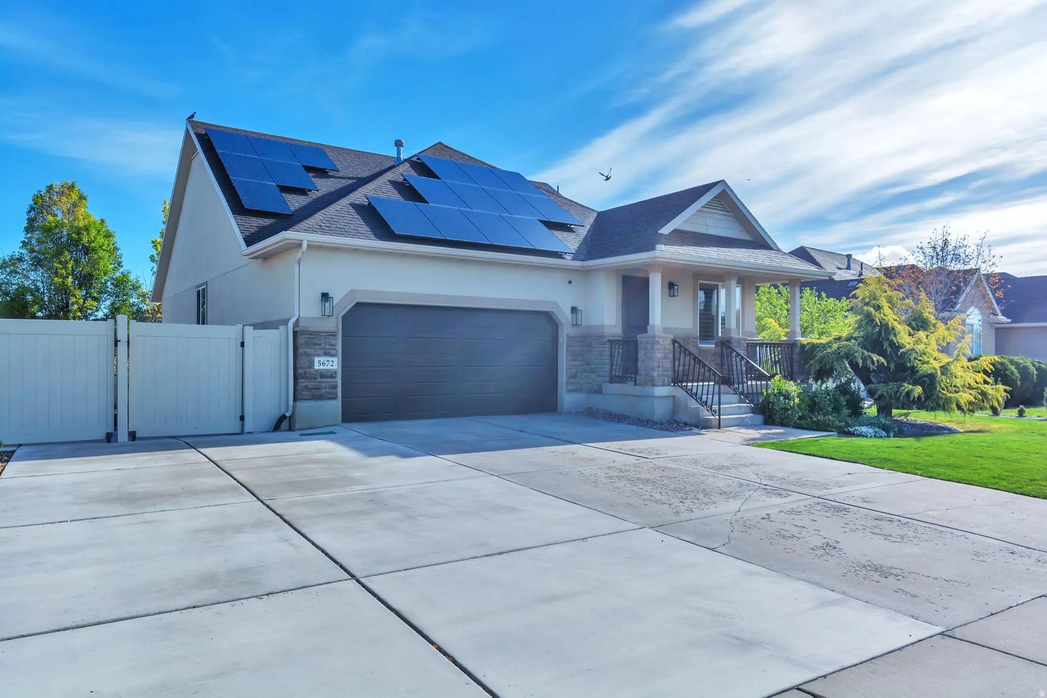 View of front facade featuring a gate, solar panels, an attached garage, stucco siding, and driveway