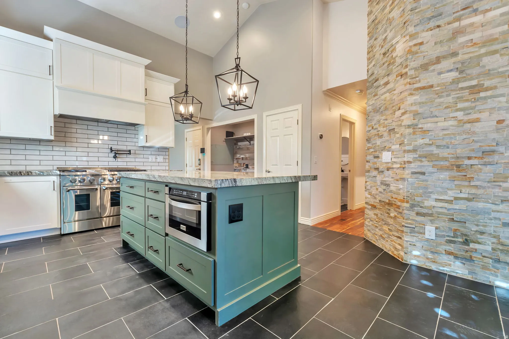 Kitchen with two tone cabinetry, a center island, stainless steel appliances, light stone counters, and suspended lighting