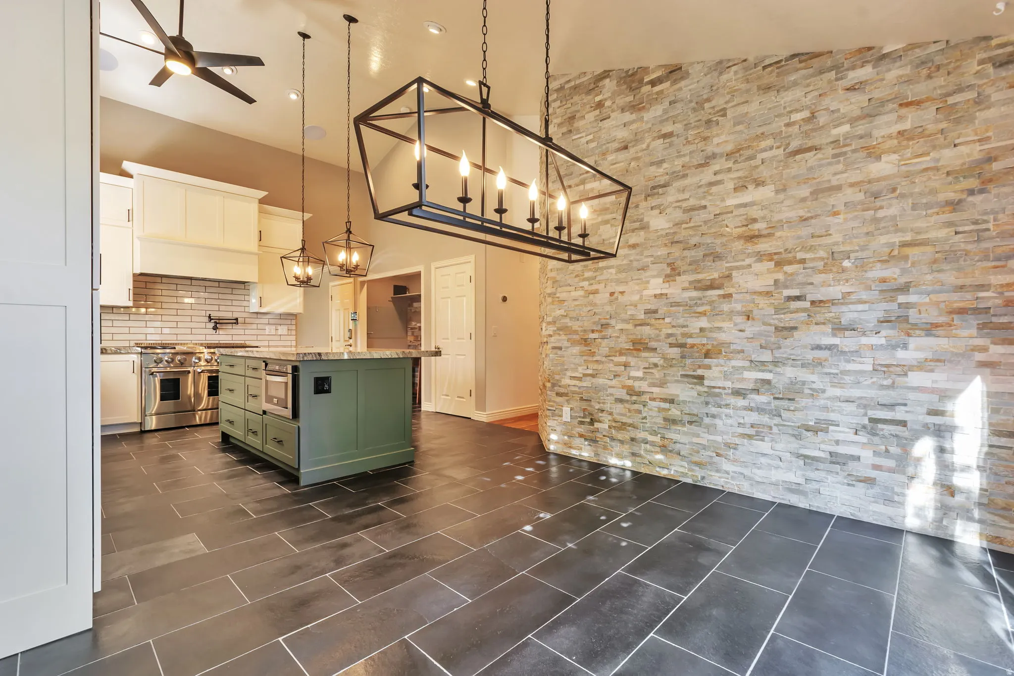 Two tone kitchen featuring two tone cabinets, a center island, light stone counters, hanging lights, and ceiling fan