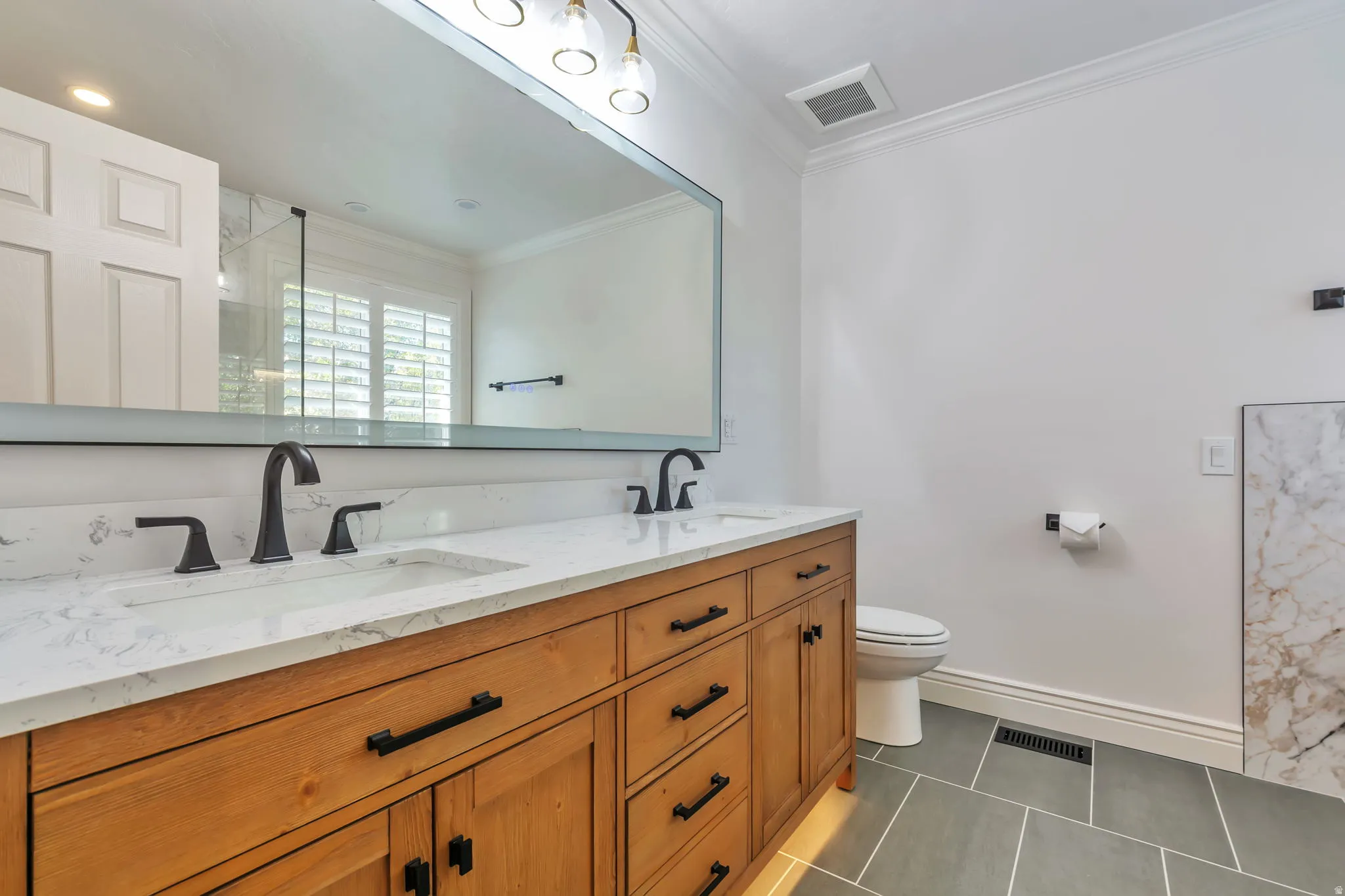 Full bath featuring ornamental molding, double vanity, dark tile patterned floors, and a shower stall