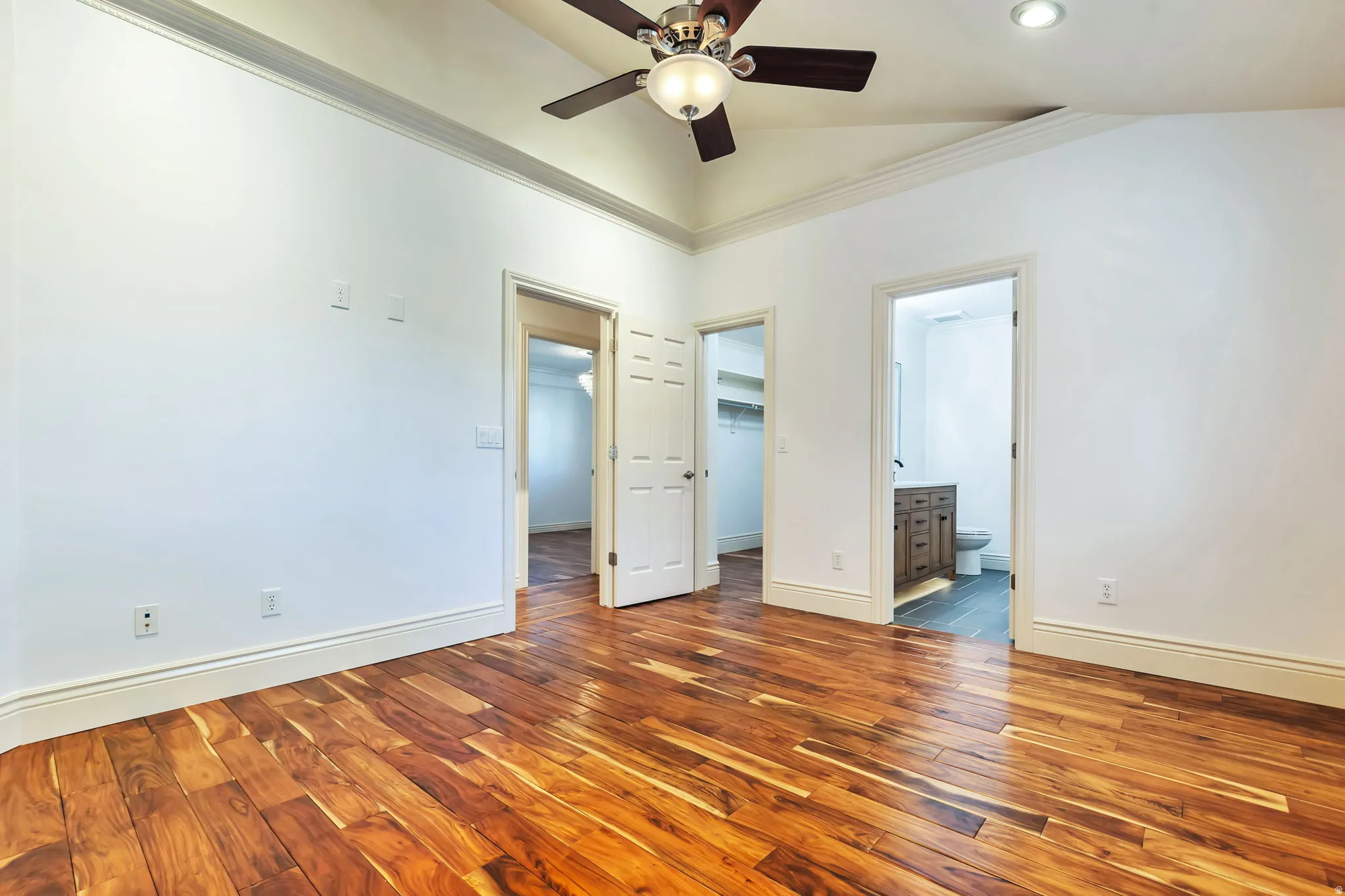 Unfurnished bedroom with dark wood-type flooring, a walk in closet, ornamental molding, ceiling fan, and ensuite bath
