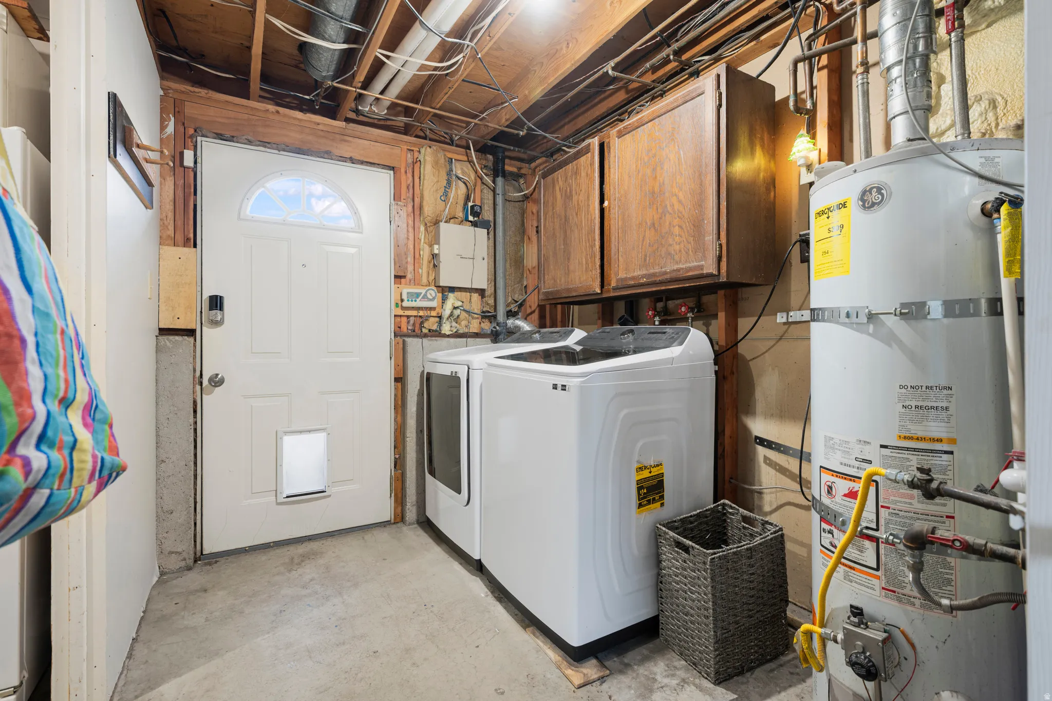 Laundry area with unfinished concrete floors, strapped water heater, washer and clothes dryer, cabinet space, and electric panel