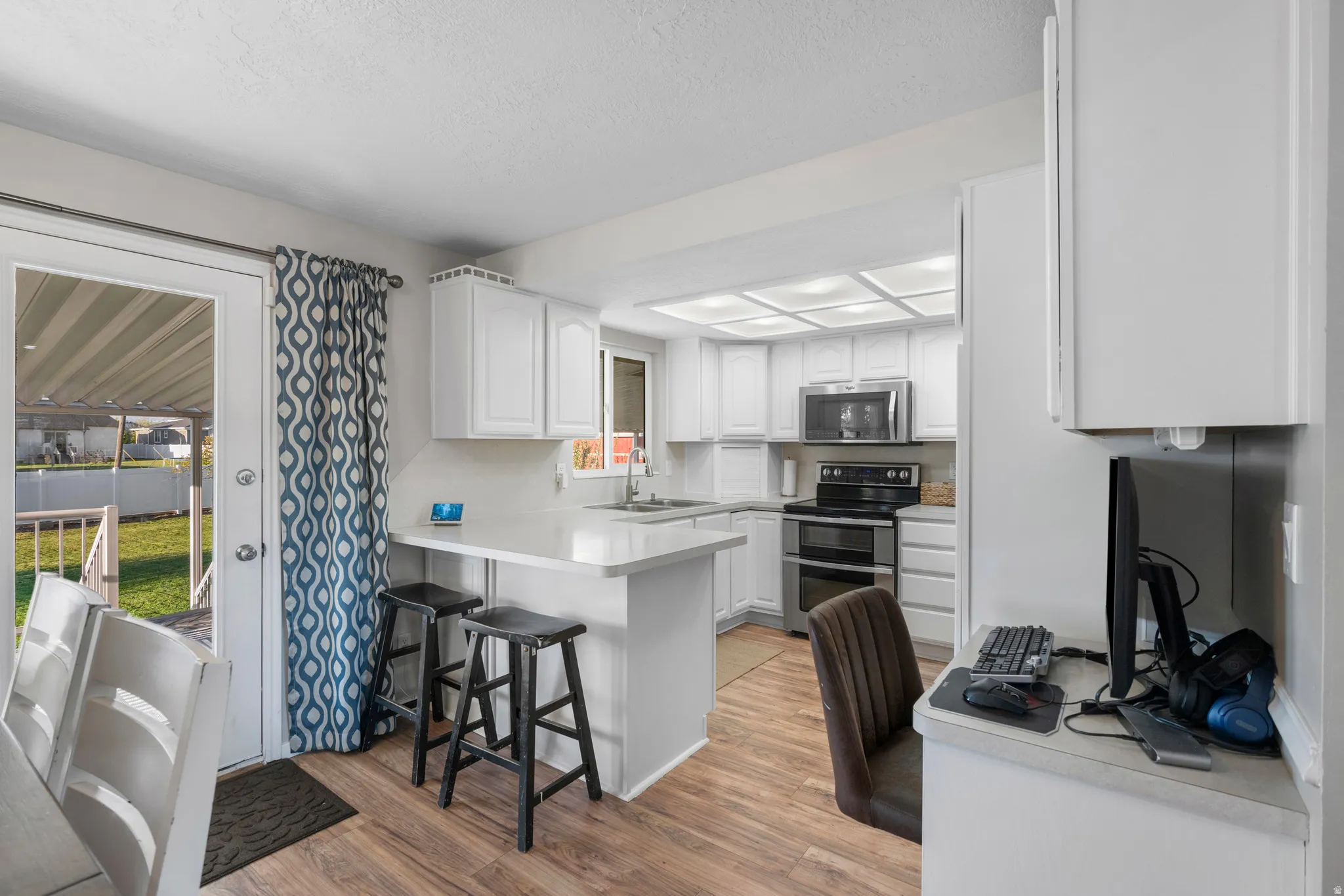 Kitchen with white cabinets, a peninsula, light countertops, stainless steel appliances, and light wood-type flooring