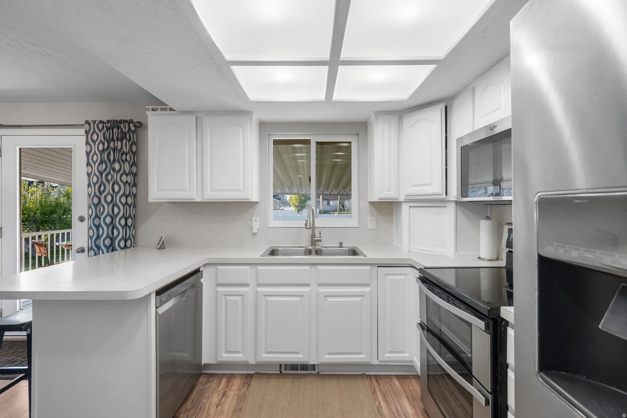 Kitchen featuring a peninsula, stainless steel appliances, a kitchen bar, light countertops, and white cabinetry