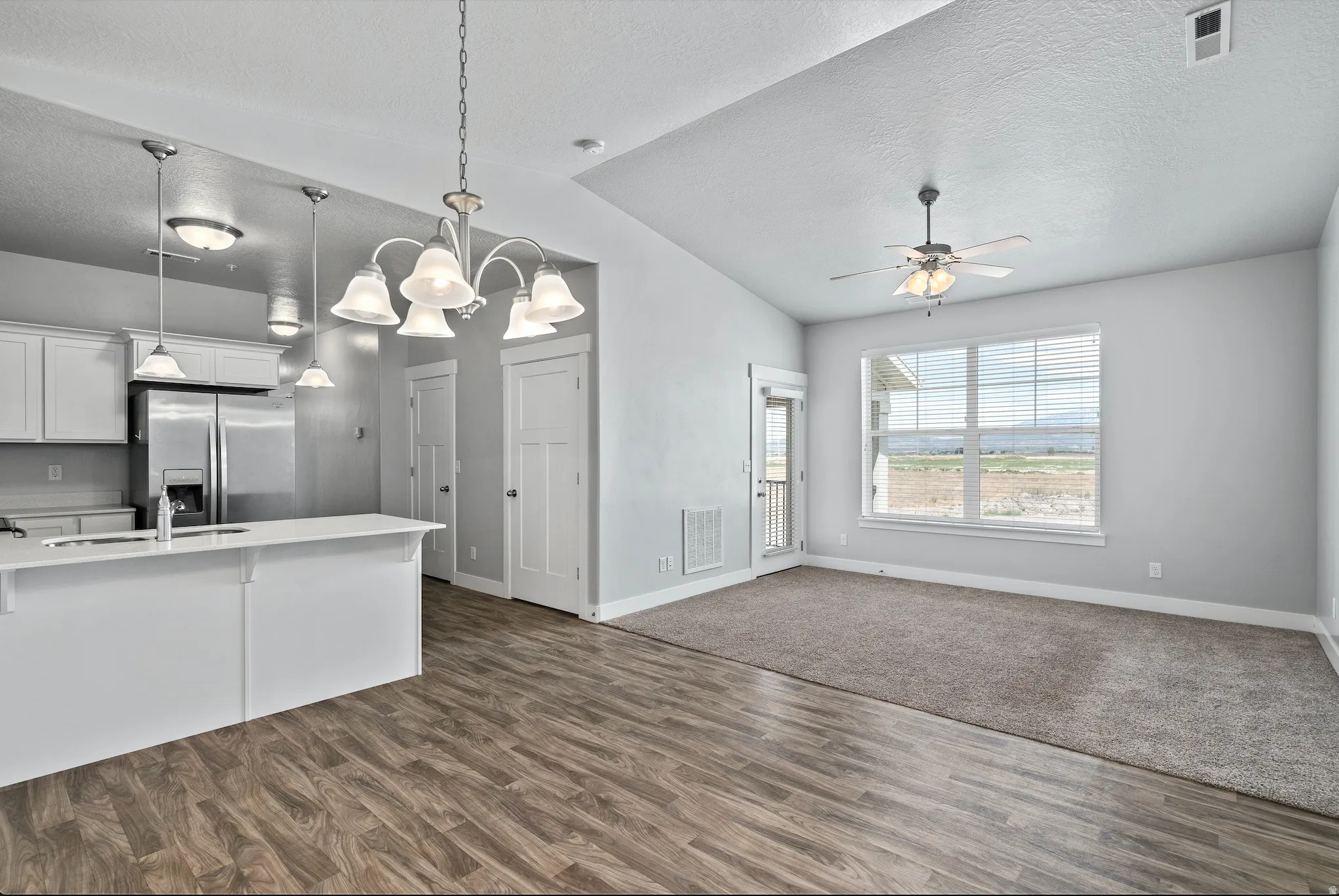 Kitchen featuring white cabinets, suspended lighting, stainless steel refrigerator with ice dispenser, open floor plan, and ceiling fan