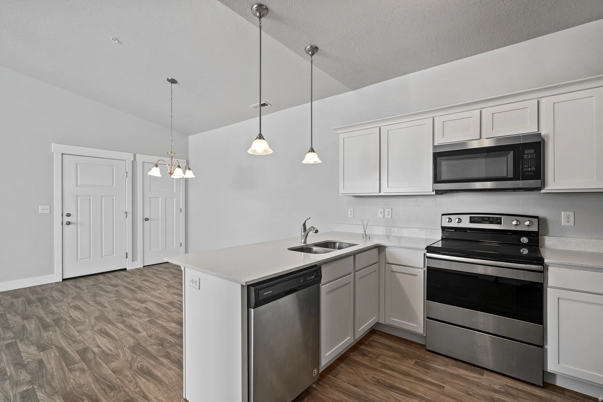 Kitchen featuring stainless steel appliances, a peninsula, dark wood-type flooring, hanging lights, and lofted ceiling