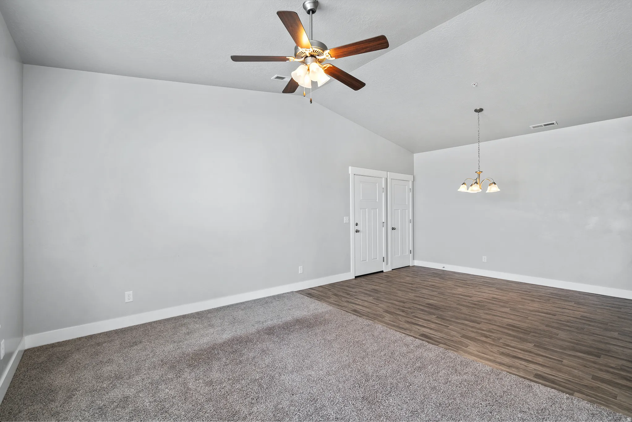 Spare room featuring ceiling fan, suspended lighting, dark colored carpet, and dark wood-style floors