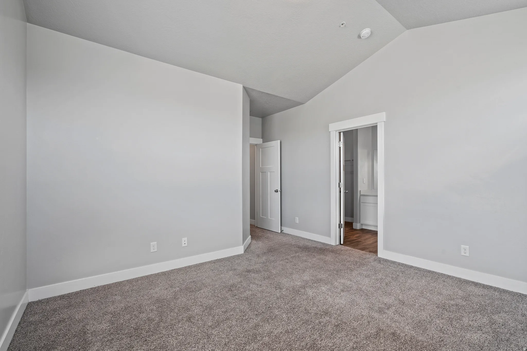 Unfurnished bedroom featuring lofted ceiling, carpet, and ensuite bath